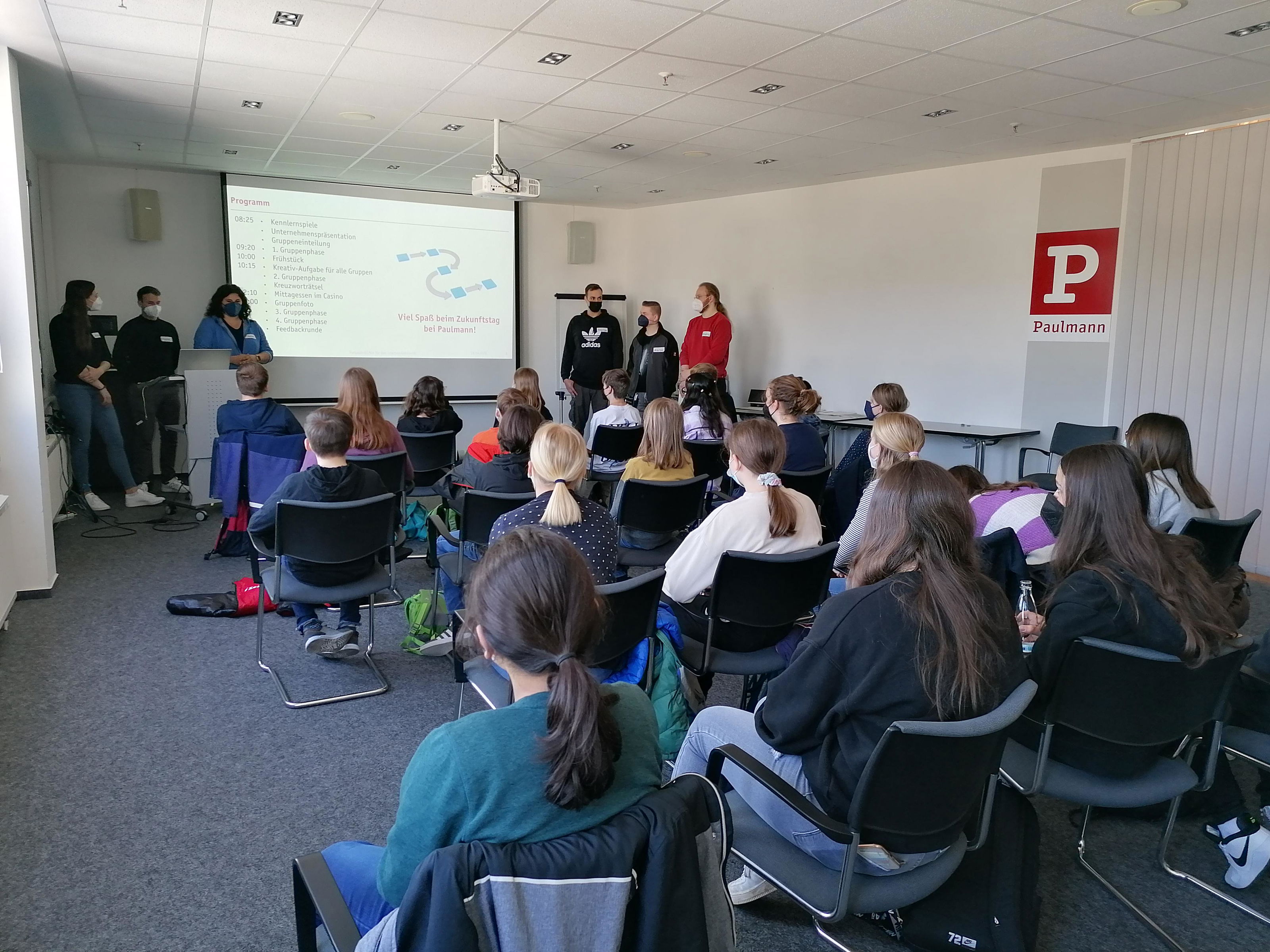 Gruppe junger Menschen bei Präsentation im Seminarraum mit Paulmann-Logo und Projektor für Ausbildungstag.