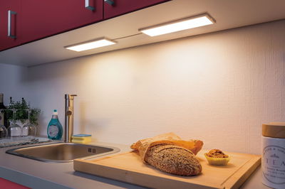 Kitchen countertop with stainless steel sink, wooden cutting board, bread, and warm white LED under-cabinet lights.