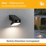 Zwarte solar buitenwandlamp met bewegingssensor op grijze muur, energiezuinige LED-verlichting