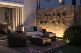 Gezellige tuinlounge met polyrattan meubels en LED-vloerverlichting op houten terras bij schemerlicht