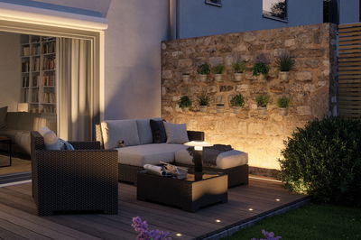 Gemütliche Gartenlounge mit Polyrattan-Möbeln und LED-Bodenbeleuchtung auf Holzterrasse bei Abendlicht