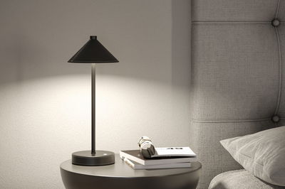 Lampe de table noire en métal avec abat-jour conique sur table de chevet grise près d’une tête de lit rembourrée.