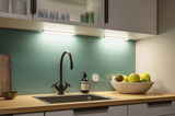 Plan de travail de cuisine moderne avec robinet noir, surface en bois et éclairage LED sous meuble.