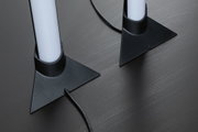Zwei weiße LED-Leuchten mit schwarzer dreieckiger Kunststoffbasis auf dunklem Holztisch, Kabel sichtbar