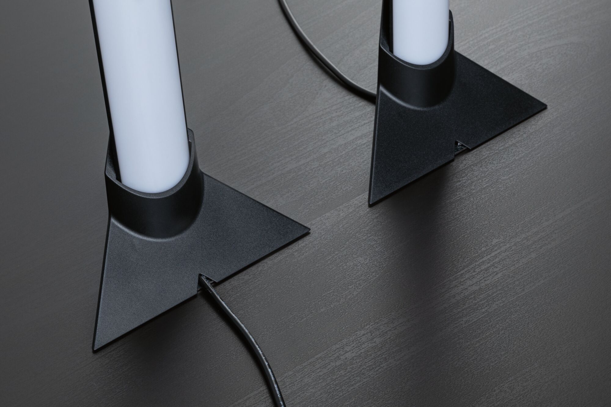 Zwei weiße LED-Leuchten mit schwarzer dreieckiger Kunststoffbasis auf dunklem Holztisch, Kabel sichtbar