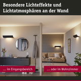 Moderne Wandlampen in Schwarz erzeugen warme Lichteffekte im Eingangsbereich und Wohnzimmer.