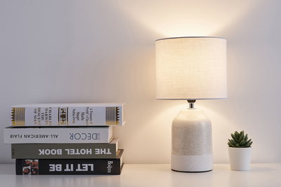 Lampe de table en céramique crème avec abat-jour en tissu clair à côté de livres et petite plante succulente verte