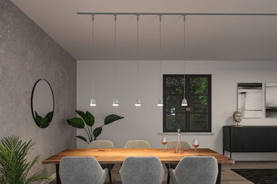 Moderne weiße Pendelleuchten aus Metall über Holztisch in Esszimmer mit grauen Stühlen und Pflanzen