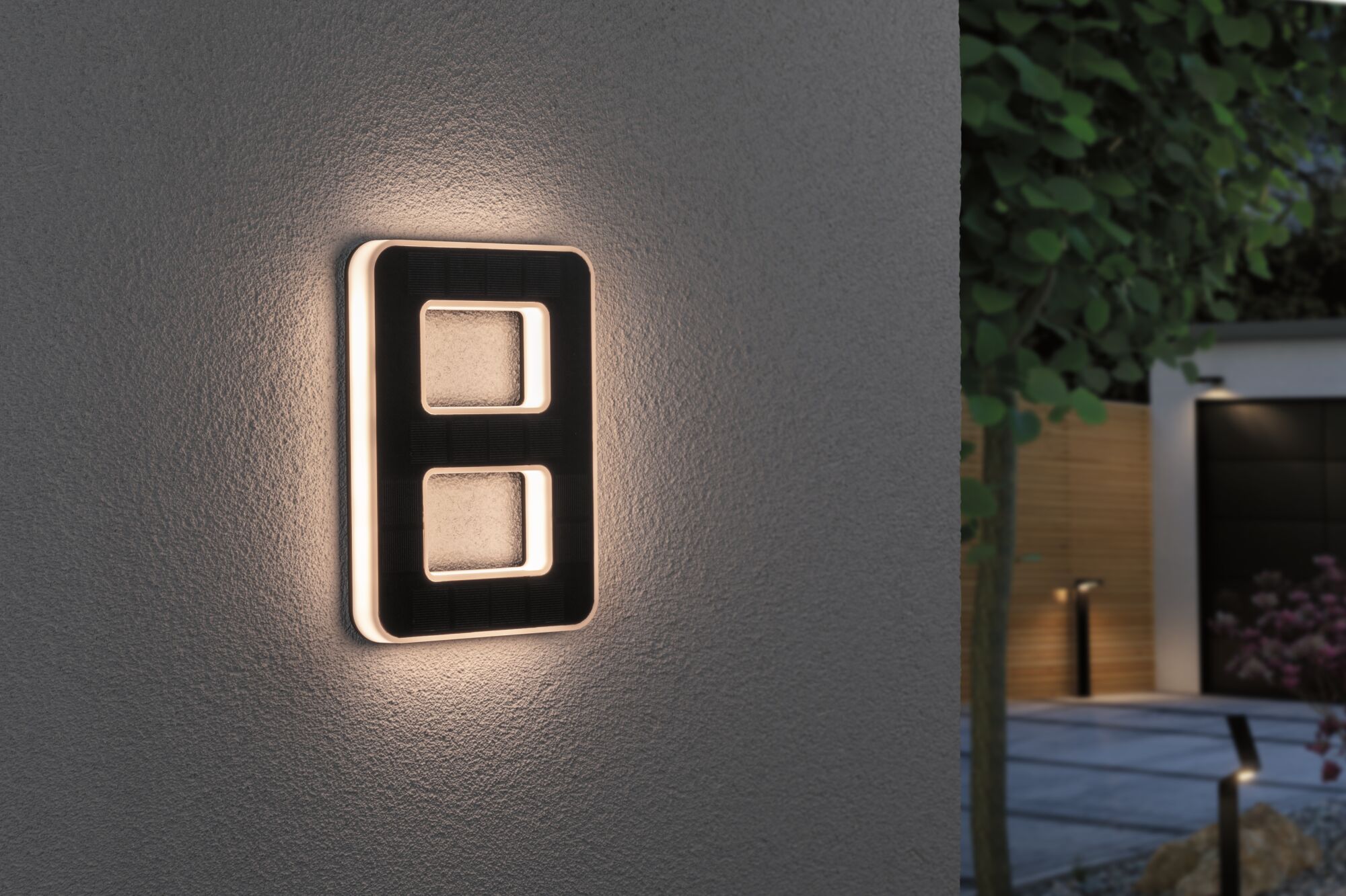 Modern black LED wall light with warm white illumination on exterior wall in garden setting