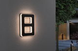 Modern black LED wall light with warm white illumination on exterior wall in garden setting