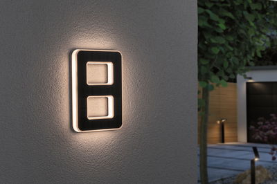 Modern black LED wall light with warm white illumination on exterior wall in garden setting
