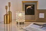 Decorative table lamp with textured glass and gold metal base beside gold candle holders and picture frames