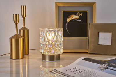 Decorative table lamp with textured glass and gold metal base beside gold candle holders and picture frames