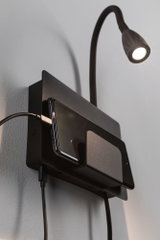 Zwarte wandlamp met flexibele arm en metalen telefoonhouder, ideaal voor slaapkamerverlichting en opladen.