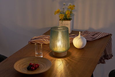 Groene glazen tafellamp met houten voet op houten tafel, versierd met keramische vaas en fruitschaal