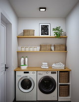 Moderne weiße Waschmaschine und Trockner mit Holzarbeitsplatte und geflochtenen Körben in heller Waschküche