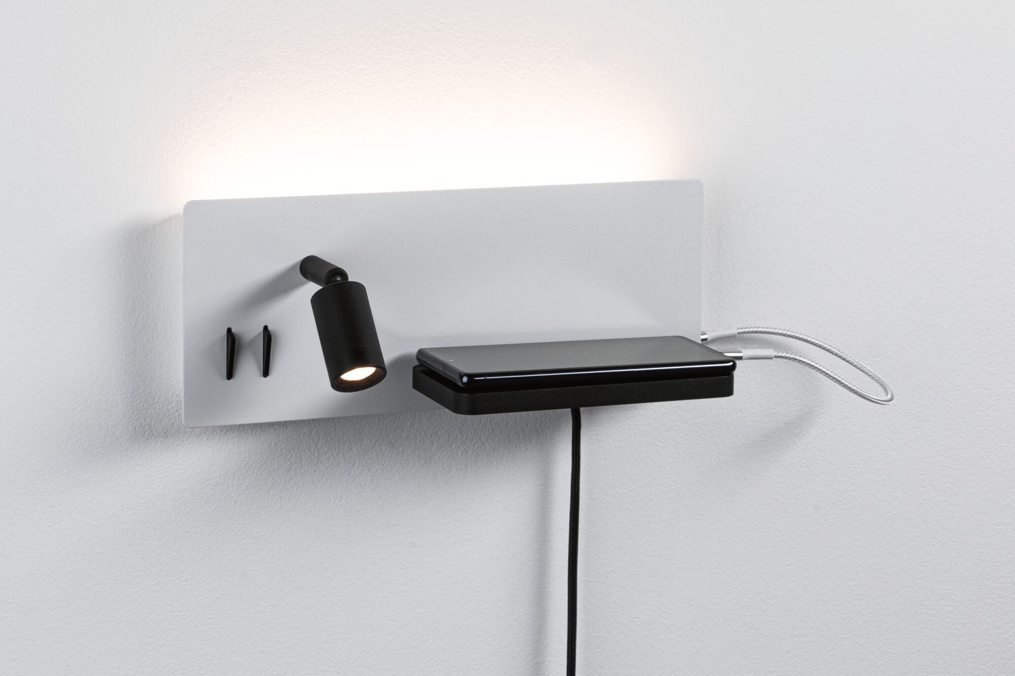 Moderne witte wandlamp met zwarte LED-spot en plankje voor smartphone met USB-laadkabels