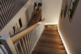 Escalier en bois moderne avec rambarde blanche et éclairage LED indirect sur le mur dans un espace de vie.