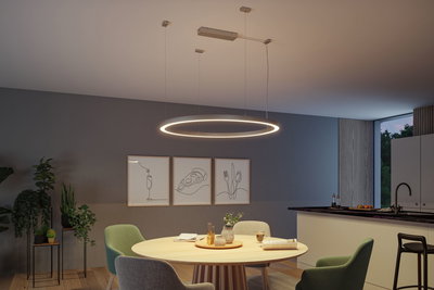 Modern round LED pendant light in warm white above wooden dining table with green chairs