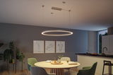 Modern round LED pendant light in warm white above wooden dining table with green chairs