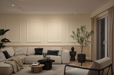 Moderne woonkamer met beige hoekbank, zwarte en grijze kussens, houten salontafels en groene planten