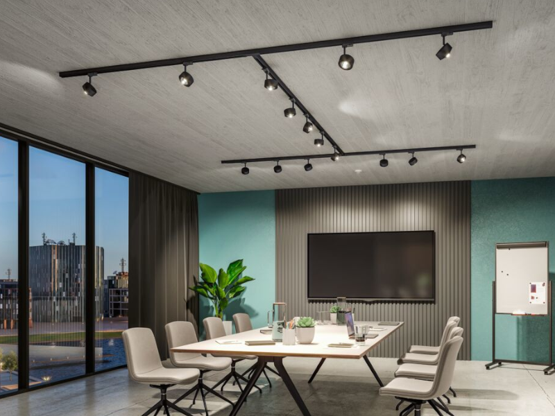 Modernes Besprechungszimmer mit schwarzer Schienenbeleuchtung, großem Bildschirm und grauen Stühlen.