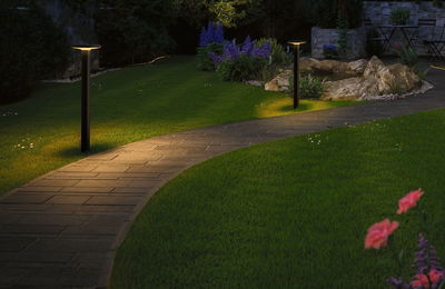 Modern black metal LED pathway light with warm white illumination along garden path at night.