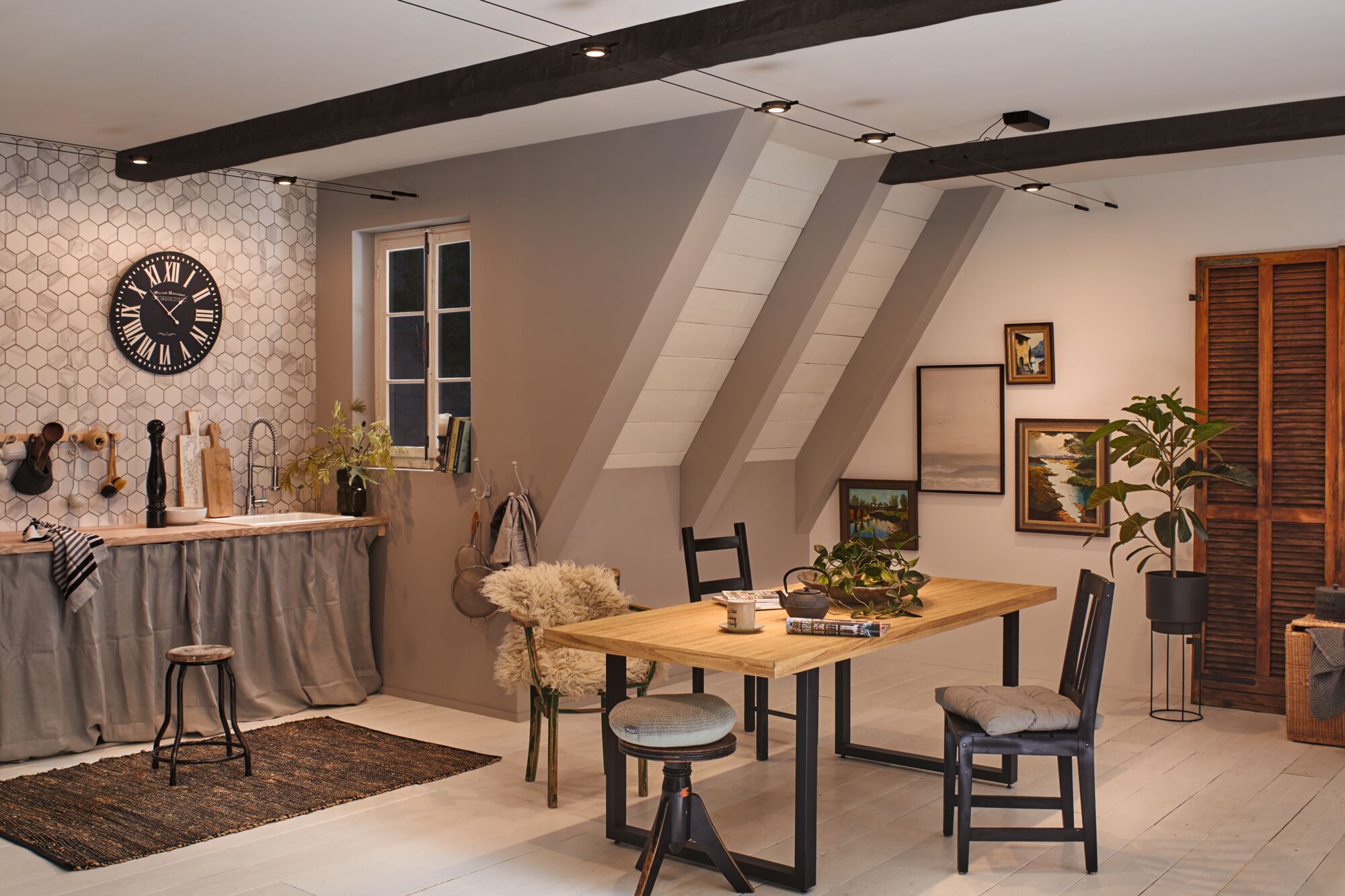 Moderne keuken met houten eettafel, zwarte stoelen en kabelspots aan het plafond voor accentverlichting