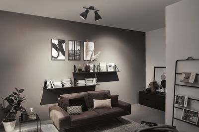 Moderner Wohnraum mit schwarzer Deckenleuchte aus Metall, grauer Wand und braunem Sofa mit Kissen