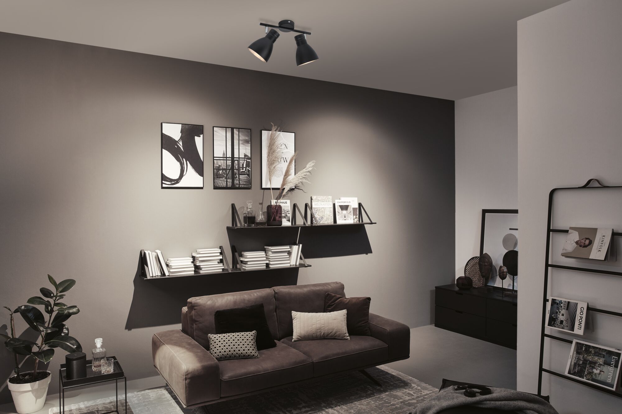 Moderne woonkamer met zwarte metalen plafondlamp, grijze muur en bruine bank met kussens