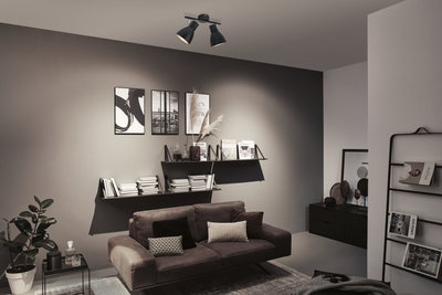 Moderner Wohnraum mit schwarzer Deckenleuchte aus Metall, grauer Wand und braunem Sofa mit Kissen