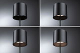 Quatre vues d'une lampe sur pied noire en métal avec abat-jour cylindrique et lumière blanc chaud.