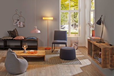 Gemütliches Wohnzimmer mit grauem Sitzsack, blauer Stuhl und Hocker, Holzregal und warmen Leuchten