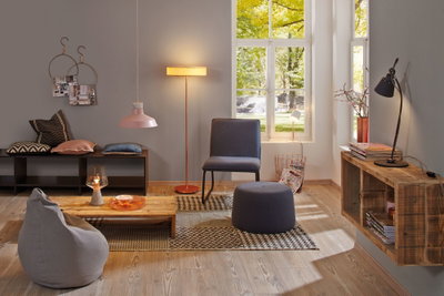 Gemütliches Wohnzimmer mit grauem Sitzsack, blauer Stuhl und Hocker, Holzregal und warmen Leuchten