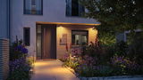 Beleuchteter Hauseingang mit moderner Außenbeleuchtung und blühendem Garten am Abend