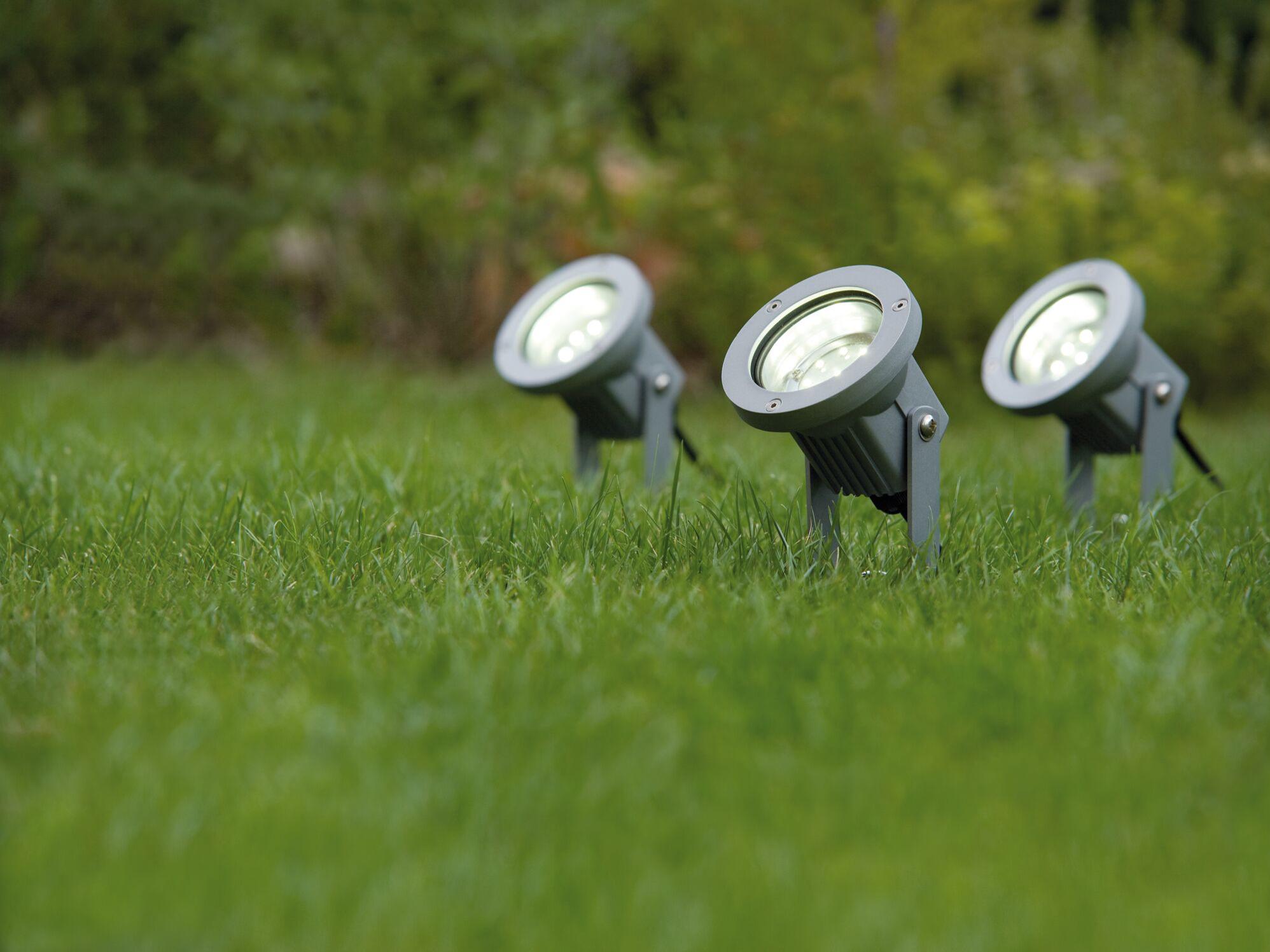 Drie grijze metalen LED-grondspiesen op groen gras voor tuinverlichting en buitenlicht.