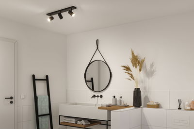 Sort loftlampe med tre justerbare spots i moderne badeværelse med hvid vask og spejl.