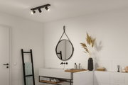 Plafonnier noir à trois spots réglables dans salle de bain moderne avec lavabo blanc et miroir.