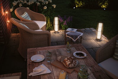 Gemütliche Terrasse mit Rattanmöbeln und warmweißen LED-Außenleuchten für stimmungsvolle Gartenbeleuchtung.
