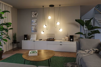 Moderne Wohnzimmerbeleuchtung mit fünf hängenden Kugelleuchten in warmweißem Licht und grünem Kabel.