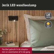 Zwarte Jerik LED wandlamp met warm wit licht aan houten wand naast bed met groen kussen