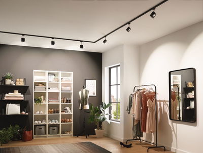 Modern dressing room with black track lighting and clothing rack with dresses under warm lighting