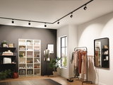 Modernes Ankleidezimmer mit schwarzer Schienenbeleuchtung und Garderobe mit Kleidern in warmem Licht