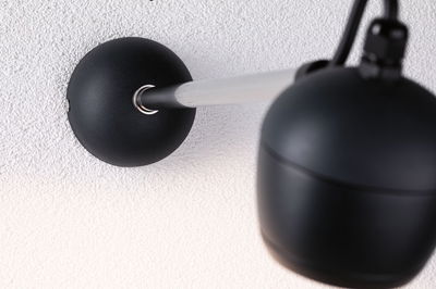 Black wall lamp with matte metal arm and spherical shade on white wall for modern lighting design