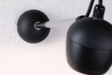 Black wall lamp with matte metal arm and spherical shade on white wall for modern lighting design