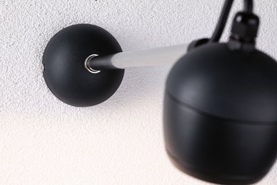Black wall lamp with matte metal arm and spherical shade on white wall for modern lighting design