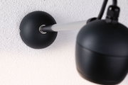 Black wall lamp with matte metal arm and spherical shade on white wall for modern lighting design