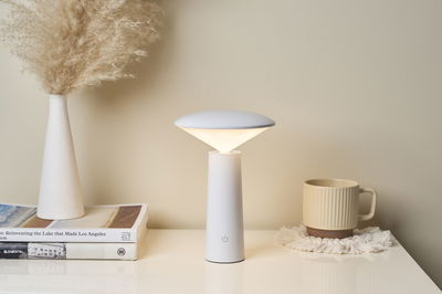 Modern white LED table lamp with conical base and warm white light on bright table with decor.