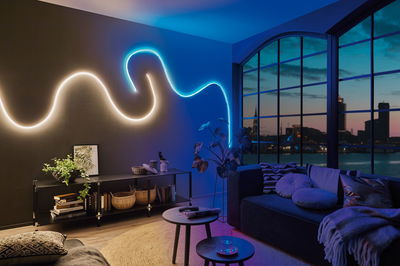 Living room with modern white and blue LED wall lighting, stylish furniture including sofa and large windows.