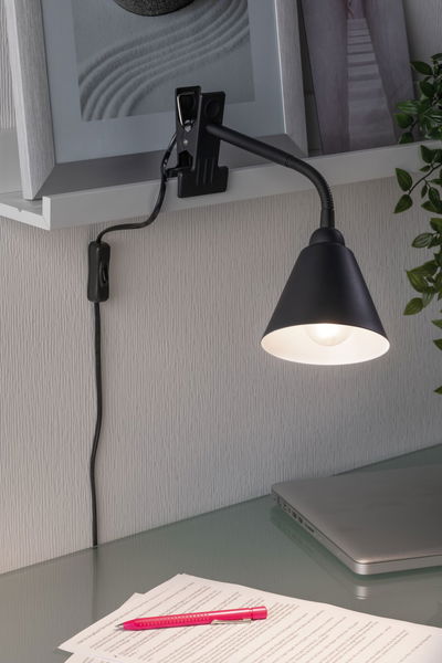 Black clamp lamp with flexible arm on white shelf, lighting desk with laptop and papers for reading.